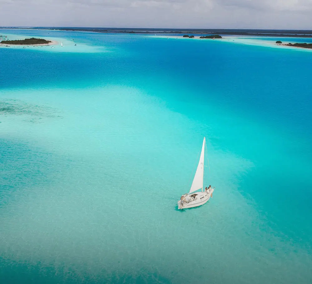A white sailboat on shallow turquoise water over pale sand.