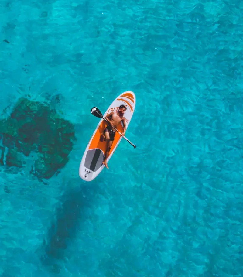 Seen from above, a paddleboarder on clear turquoise water.